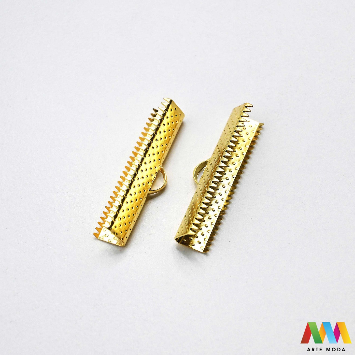 Metalni stiskači i završeci sa zubima za izradu nakita u srebrnoj, zlatnoj i brončanoj boji složeni na radnoj površini. Prikazani su ravni stiskači za tekstilne trake, baršun, antilop i plosnate kožice s integriranom omčicom za spajanje s kopčama i produžnim lančićima. Kvalitetan repromaterijal za uredno fiksiranje krajeva pri izradi choker ogrlica, narukvica i modnih dodataka u DIY radionicama za ručnu izradu unikatnog nakita s nazubljenim rubovima koji jamče čvrst prihvat bez ispadanja materijala.